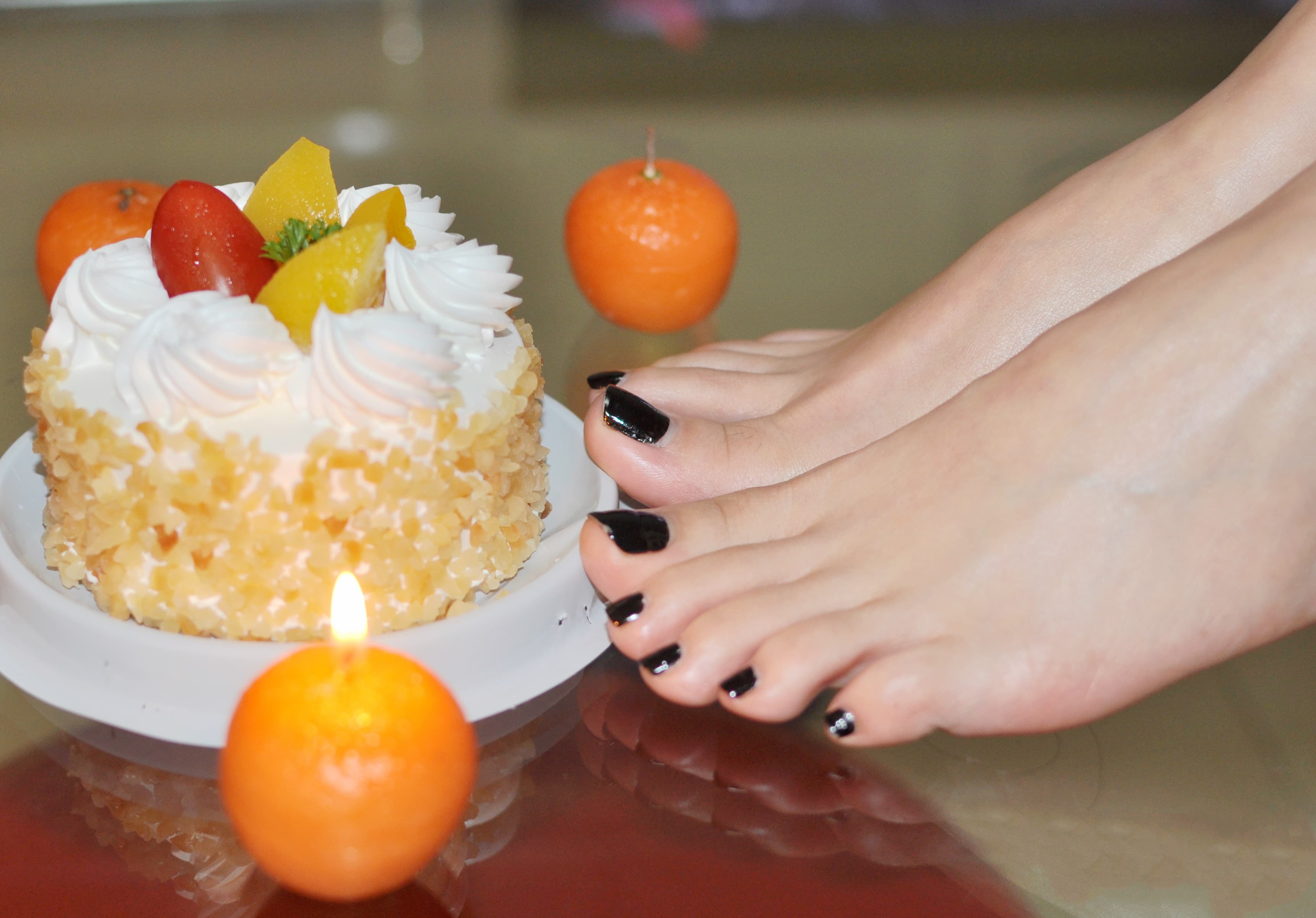 Festive close-up of decorated toes and a stockinged foot near cake frosting, playful party confetti scattered on a wooden table.
